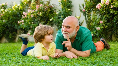 Familienplanung Ü60 - Sind alte Väter gute Väter. Mann und Kleinkind liegen auf einer Wiese